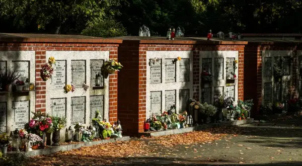 Kamienna ściana na urny z prochami, ozdobiona kwiatami i zniczami, otoczona jesiennymi liśćmi.