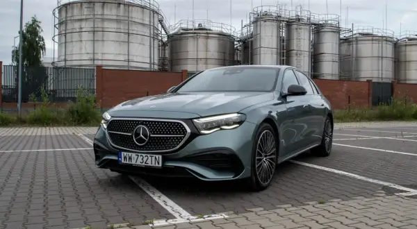 Nowy Mercedes E220d w kolorze zielonym, zaparkowany przed przemysłowymi zbiornikami.