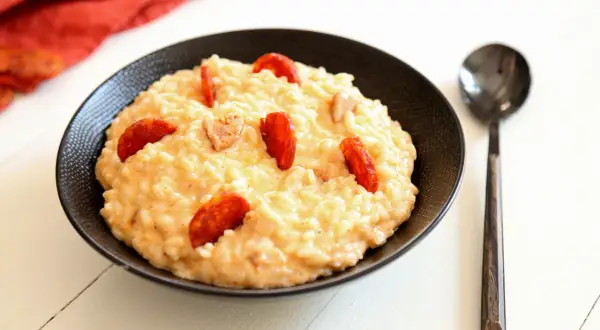 Un crémeux risotto chorizo, garni de rondelles de saucisse épicée, servi dans un bol noir avec une cuillère.