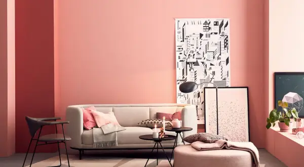 Gemütliches Wohnzimmer mit einer rosa Wand, einem hellen Sofa, Kissen und einem runden Hocker.