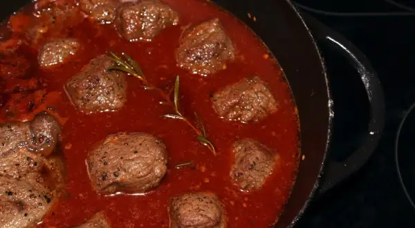 Stracotto di manzo schmort in einer tiefroten Sauce mit Rosmarin. Zarte Fleischstücke, perfekt für ein herzhaftes Gericht.
