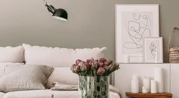 Gemütliches Wohnzimmer mit skandinavischen Wandfarben, einem Sofa mit Leinenkissen, Tulpen und minimalistischer Kunst.