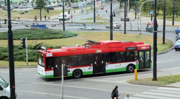 Czerwony trolejbus z napisem "Lublin" przejeżdża przez skrzyżowanie. W tle widać ruch uliczny i budynki.