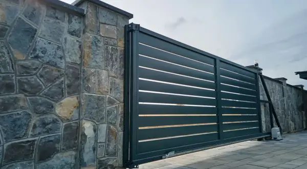Portail coulissant moderne, presque entièrement ouvert à 120 degrés, longeant un mur de pierres brutes.