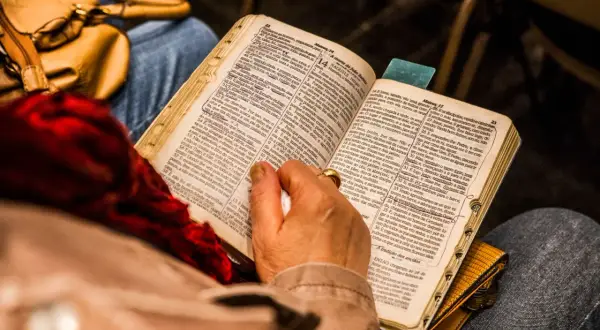Osoba czyta Biblię, skupiając się na psalm 9. W tle widać torebkę i fragmenty ubrania.