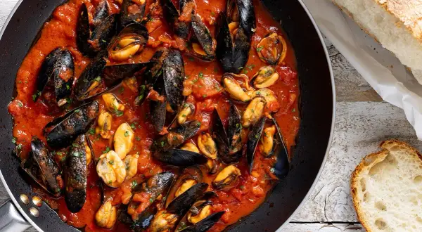 Cozze alla tarantina in padella, un piatto ricco di sapore con cozze succulente in salsa di pomodoro, accompagnate da pane fresco.