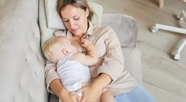 Ciepłe chwile karmienia spod pachy. Mama tuli dziecko, karmiąc je piersią na kanapie.