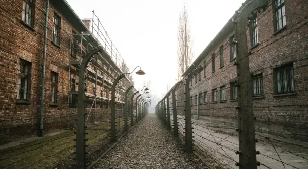 Camino de grava entre edificios de ladrillo y alambradas con espinos, evocando el triste recuerdo del autobús Cracovia Auschwitz.