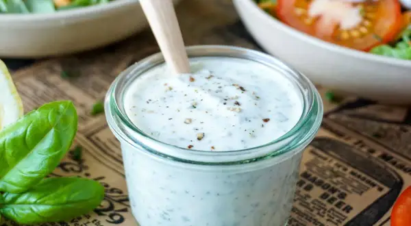 Cremiges Joghurt Dressing mit Kräutern in einem Glas, bereit für einen frischen Salat.