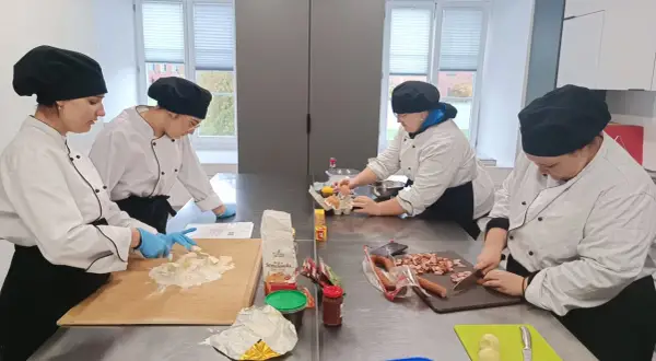 Uczniowie na kierunku technik żywienia i usług gastronomicznych ćwiczą krojenie kiełbasy i przygotowanie ciasta.