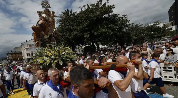 Procesión de la Virgen en las fiestas del Carmen de Foz. Hombres portan la imagen adornada con flores, mientras una multitud observa.