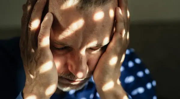 Uomo con le mani sulla testa, illuminato da fasci di luce che creano un effetto di **blocco emotivo test**.