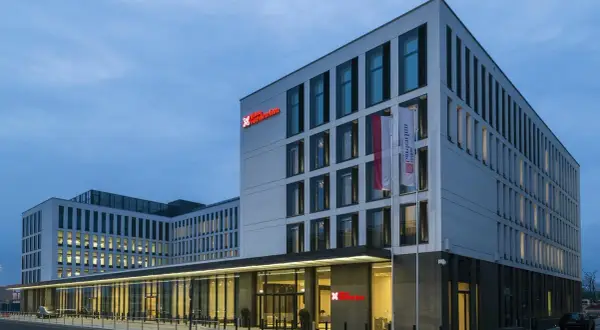 Nowoczesny budynek Hilton Garden Inn Kraków o białej fasadzie z czerwonym logo, z polską flagą przy wejściu.
