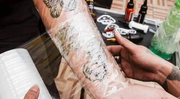 Frische tattoo wunde wird mit Folie geschützt. Tattoo-Farben und Zubehör liegen bereit.