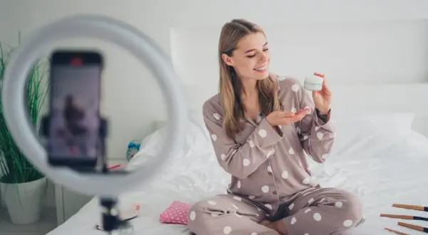 Uśmiechnięta influencerka z Polski zdradza tajemnicę egzotycznej urody, prezentując krem. Wokół kosmetyki i ring light.