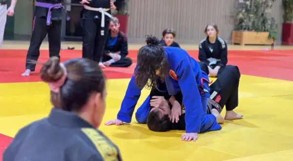 Deux pratiquants de jiu jitsu s'entraînent sur un tapis jaune et rouge. L'un est en position dominante, l'autre en défense.