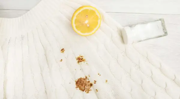 Maglione bianco con macchia di ruggine. Limone e sale pronti per rimuoverla.