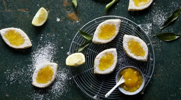 Italienische Kekse mit Lemon Curd, bestäubt mit Puderzucker, auf einem Gitter und dunklem Untergrund.