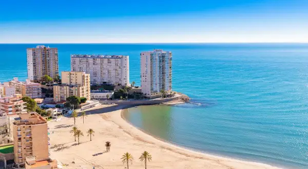 Edificios altos y una playa dorada en el balneario Cullera, con el mar azul brillante de fondo.