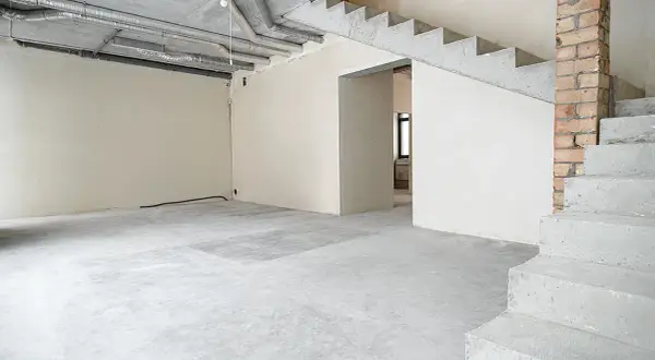 Wnętrze domu w stanie deweloperskim. Betonowe schody, ściany z tynkiem, widoczne instalacje i przewody.