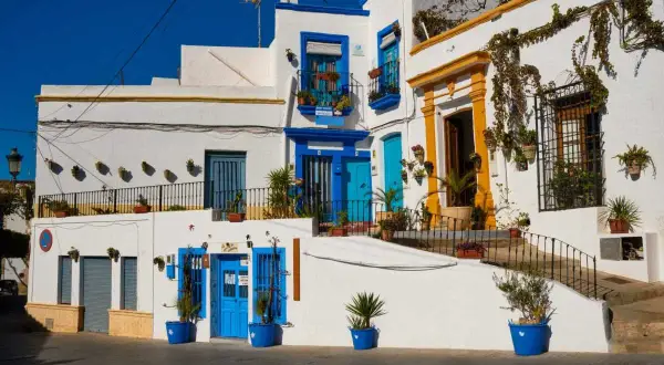 Casas blancas con puertas y ventanas azules, un ejemplo de lo que ver cerca de Níjar. Plantas en macetas adornan las fachadas.