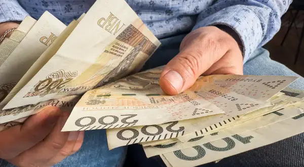 Dłonie trzymają polskie banknoty 200 zł i 100 zł. Zastanawiasz się, czy 800 plus wlicza się do dochodu?