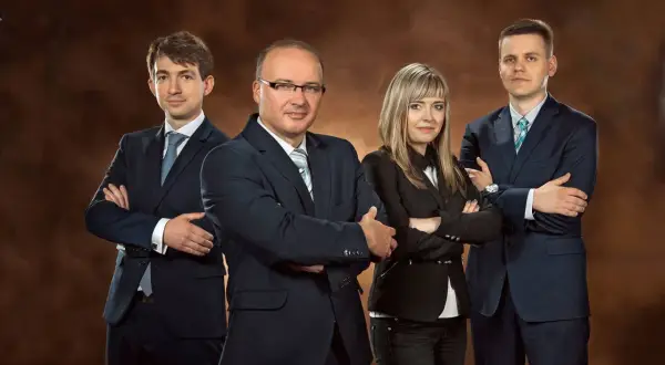 Cztery osoby w garniturach stojące z rękami skrzyżowanymi na piersi.