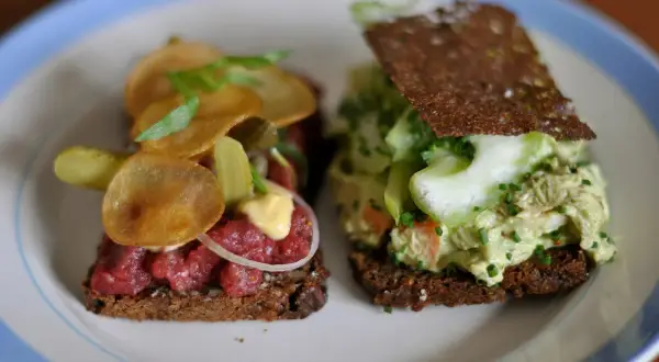 Dos sándwiches abiertos, uno con tartar de ternera y patatas fritas, otro con ensalada de pollo y pepino. Comida típica de Dinamarca.