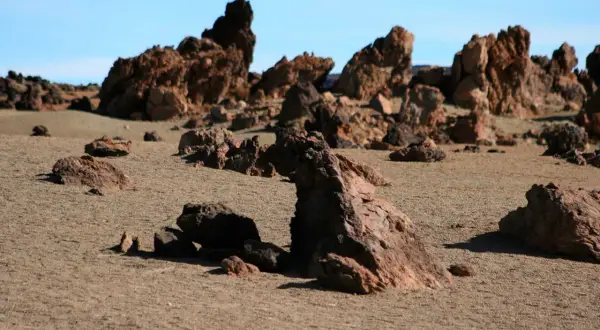 Paisaje desértico con rocas volcánicas rojizas y arena, evocando la zona de las minas de San José.
