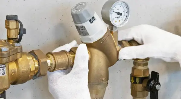 Mani guantate regolano un riduttore di pressione con manometro, mostrando come si regola la pressione dell'acqua.
