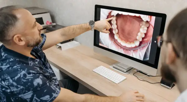 Dentysta pokazuje pacjentowi na ekranie komputera zdjęcie jamy ustnej, wskazując na zdrową kieszonkę dziąsłową.