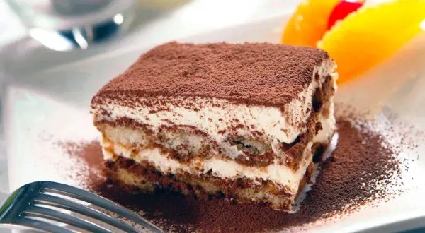 En bit krämig tiramisu, pudrad med kakao, serveras med frukt. Perfekt som dryck till tiramisu är kaffe eller en söt dessertvin.