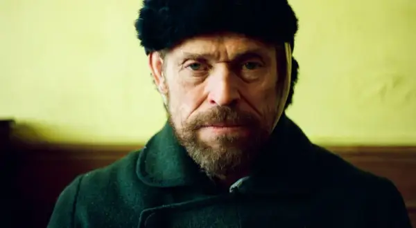Willem Dafoe w czapce z futra i ciemnym płaszczu, w kadrze z filmu.