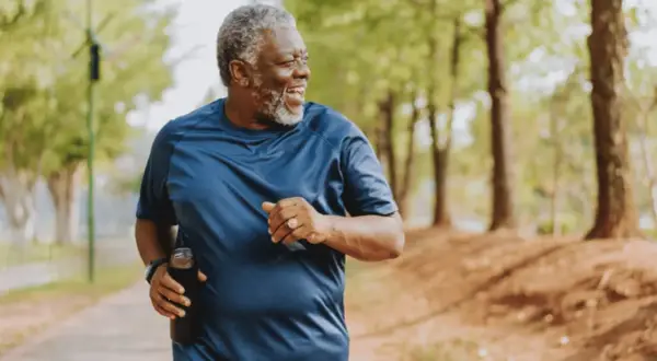 Un homme souriant court dans un parc, tenant une bouteille d'eau. Il est un exemple d'exercices pour perdre du ventre après 60 ans.
