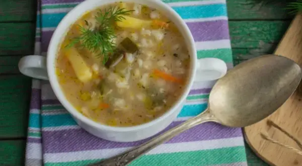 Miseczka zupy z kaszą, ziemniakami i koperkiem, obok łyżka.
