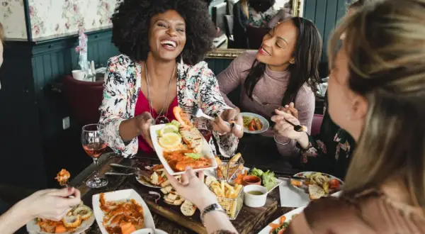 Vier Freundinnen genießen einen köstlichen Brunch in Berlin. Sie lachen und teilen sich Speisen wie Garnelen und Pommes.