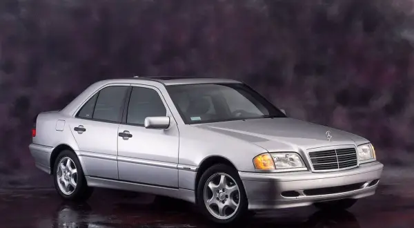 Srebrny Mercedes-Benz C-Klasa W202 z lat 90. na tle ciemnego, malowanego tła.