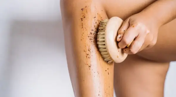 En hand använder en borste för att exfoliera benet med en brun skrubb. Det är ett bra sätt att få mjuk hud.
