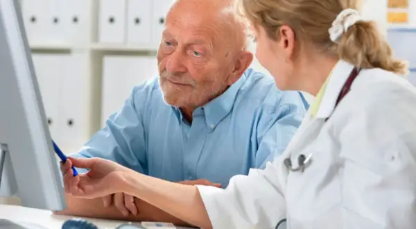 Lekarka omawia z pacjentem najnowsze leki na prostatę, wskazując na ekran komputera.