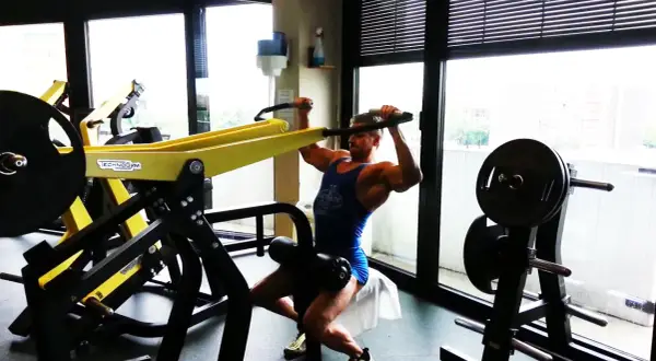 Uomo muscoloso esegue esercizi dorsali macchinari Technogym, concentrato sul movimento.