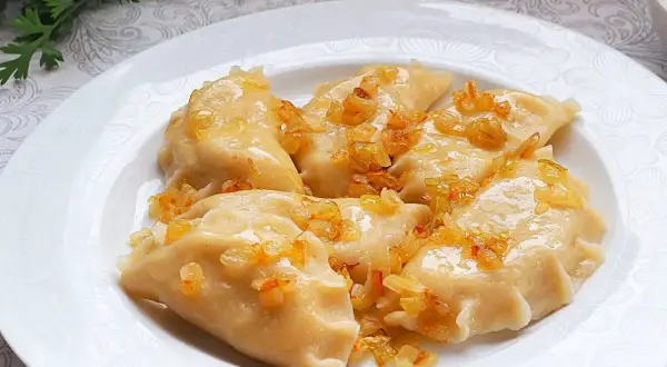 Pyszne pierogi ruskie, polane skwarkami z cebulki, na białym talerzu.