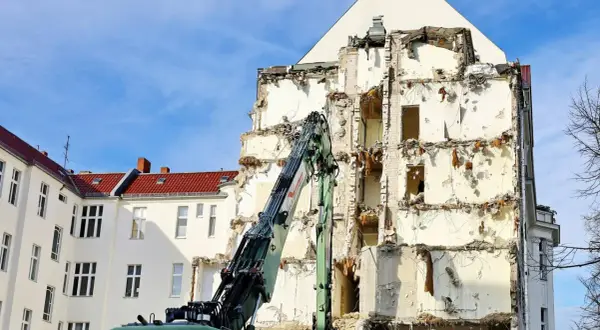 Koparka pracuje przy rozbiórce budynku, odsłaniając jego zniszczoną konstrukcję.