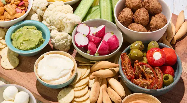 Un plateau garni pour un apéro d'été : boulettes, crudités, guacamole, fromages, olives et tomates séchées.