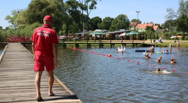 Ratownik WOPR czuwa nad bezpieczeństwem kąpiących się na Jeziorze Wielkie Skępe. Ludzie pływają i relaksują się w wodzie.