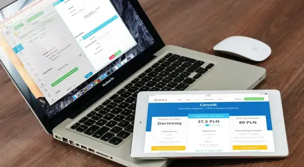 Programista .NET pracuje nad aplikacją na laptopie i tablecie. Na ekranach widoczne są formularze i cennik usług.