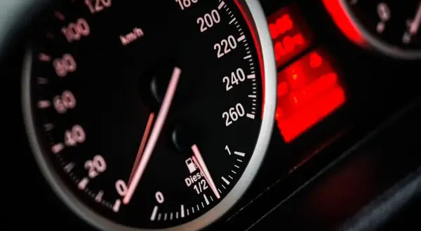 Velocímetro de coche con aguja marcando 120 km/h. El indicador de combustible marca casi lleno. Las luces de advertencia rojas brillan.