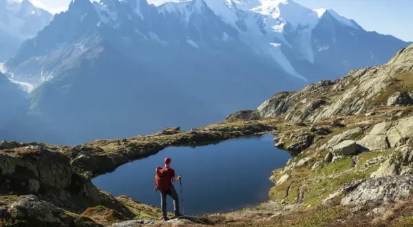 Widok na wejście na Mont Blanc. Turysta z plecakiem stoi nad górskim jeziorem, podziwiając ośnieżone szczyty.