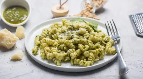 Fusilli z pesto, posypane parmezanem. Na stole widać też kawałki sera, miseczkę z sosem i słoiczek z orzeszkami pinii. Różne rodzaje makaronu mogą być równie pyszne!