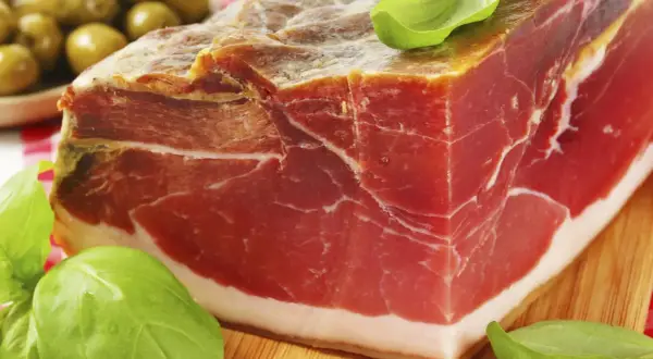 Ein Block Parma-Schinken mit zartem Fleisch und weißem Fett, garniert mit Basilikum. So sieht er aus, der echte Parma-Schinken.