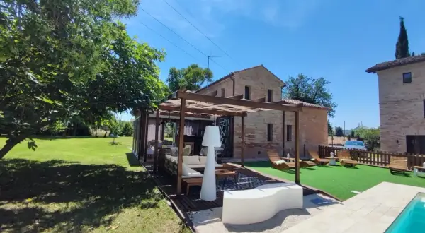 Un'oasi di relax a Poggio San Romualdo: piscina, prato verde, pergolato con divani e lettini prendisole.